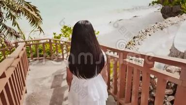 一个穿着夏季白色连衣裙的女学生正在沿着一个木制楼梯走到热带海岸。 娱乐。 夏季